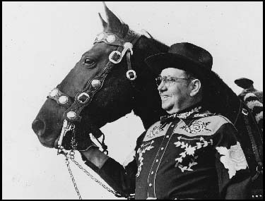 A portly, elderly gentleman wearing an outfit like Gene Autry might have worn in a 1940s western. 